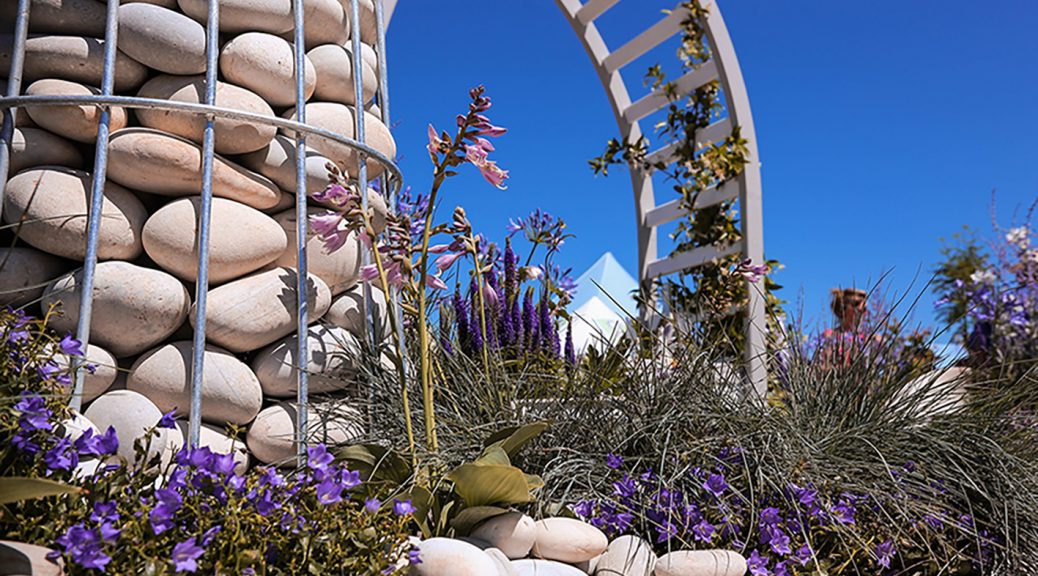 Pastel grey, blue, white cobbles in a steel framed lighthouse in a show garden with purple and green plants.