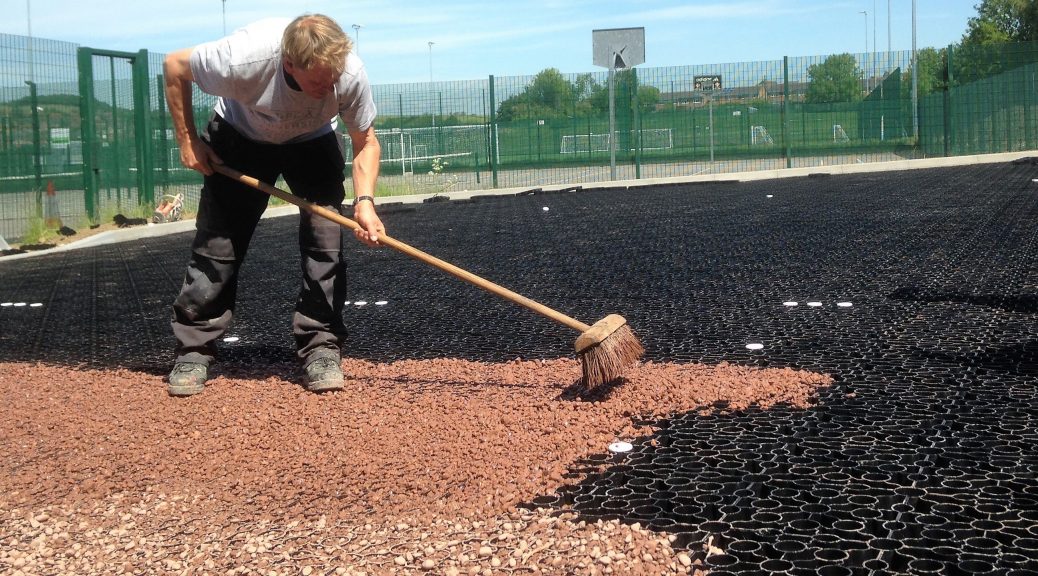 Red gravel being brushed into the gravel grid