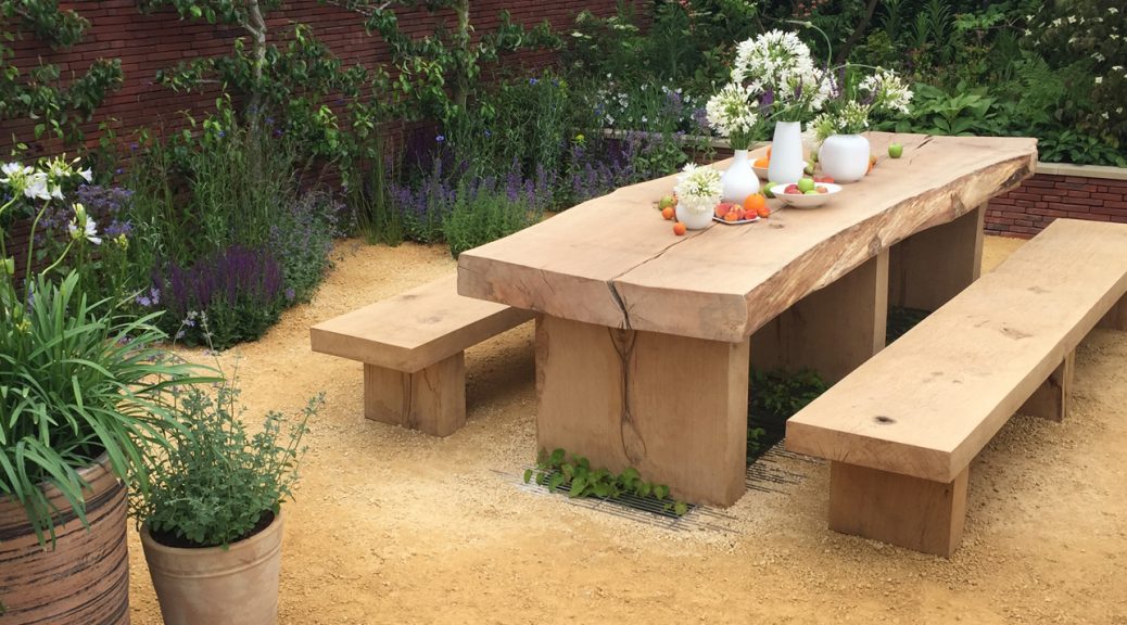 A wooden bench and table set in the Wedgwood Garden at RHS Chatsworth surrounded by brightly coloured plants.