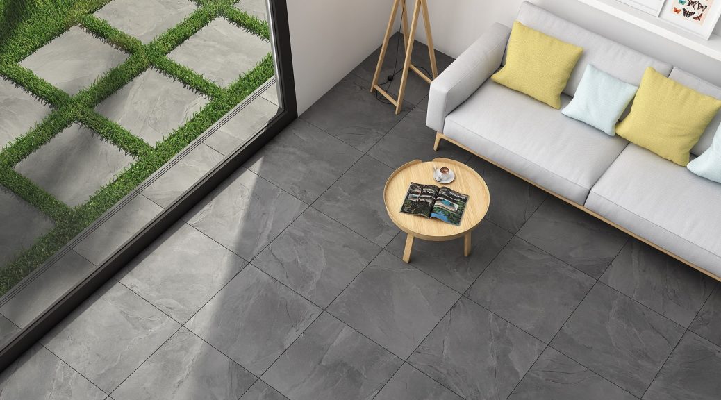 Grey paving slabs underneath a cream sofa with round wooden table.