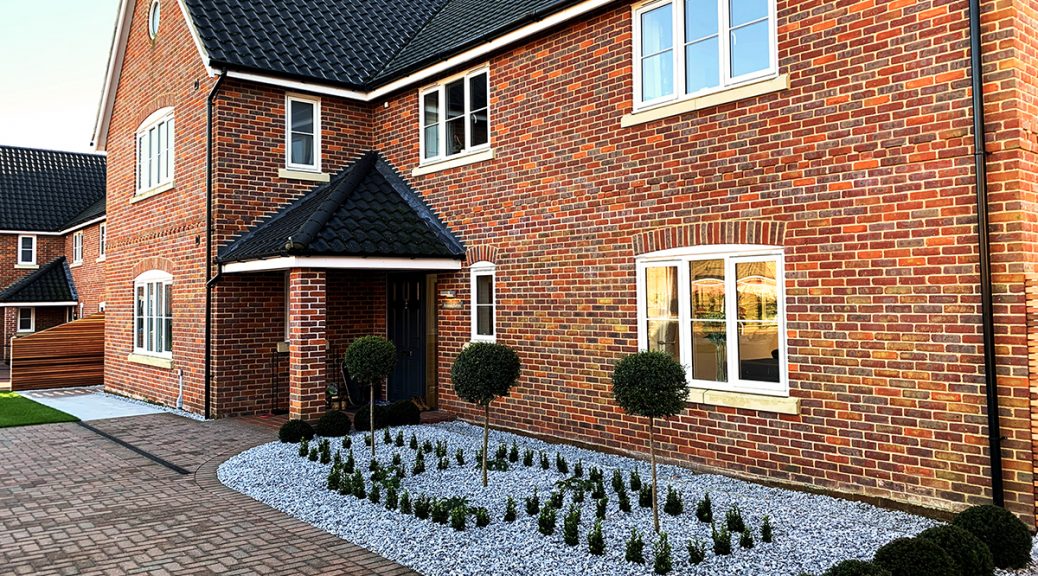 Red brick house with Ice Blue Chippings border at the front and evergreen plants dotted around.