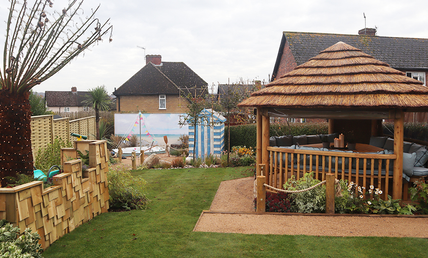 Garden with wooden shed surrounded by grass area and sand.