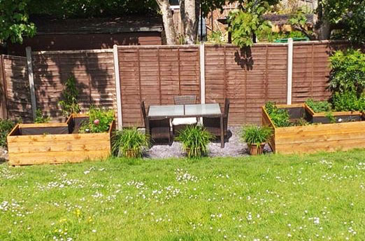Community garden with seating area surrounded by grass. Featuring raised wooden beds and slate chippings